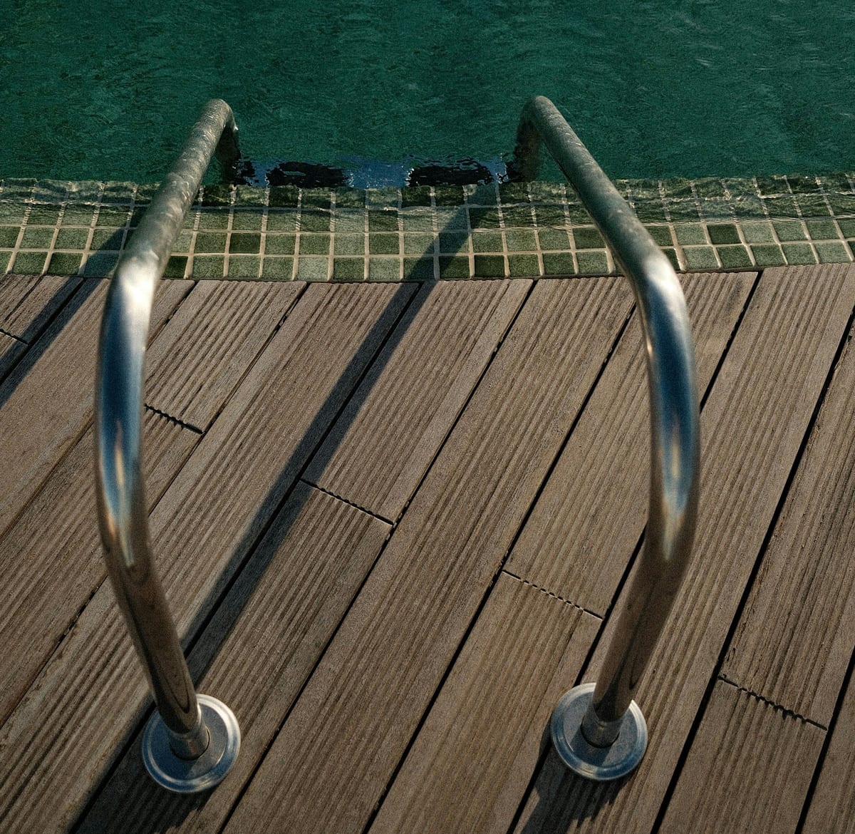 Grooved composite deck boards meeting a tiled pool edge with a chrome ladder